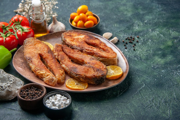 front-close-view-fried-fishes-lemon-slices-brown-plate-spices-tomatoes-oil-bottle-mix-colors-table-with-free-space_179666-18174